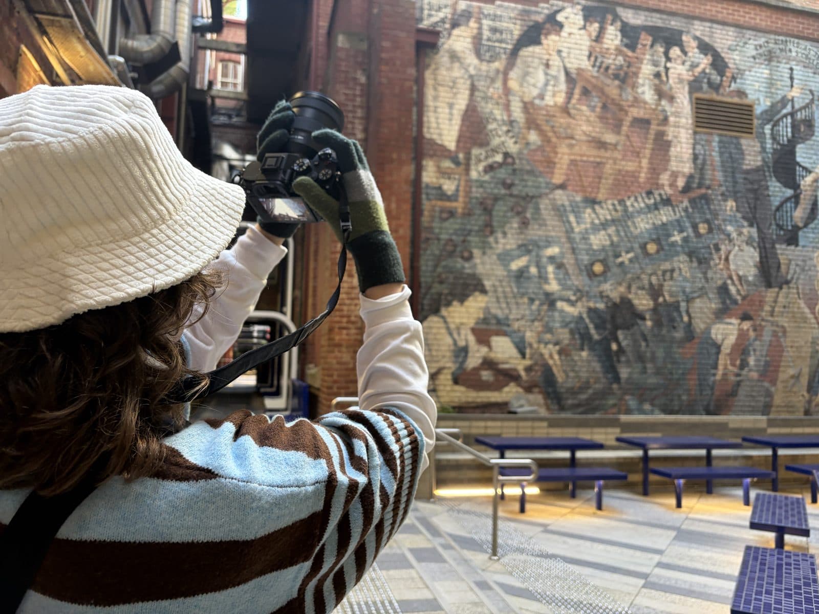 Julia photographing a large tapestry mural on a brick wall with her Sony A7 III during a Melbourne CBD photography course
