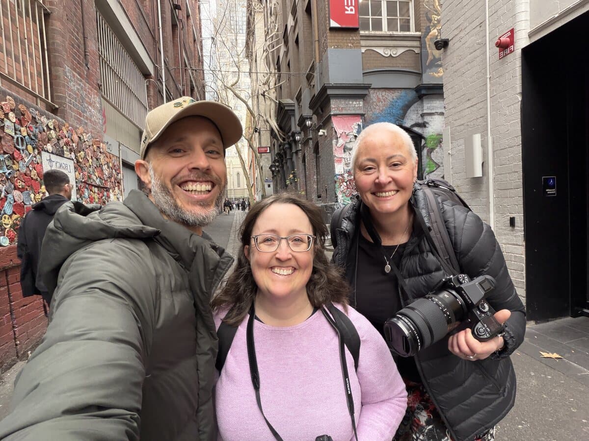 Daniel Bilsborough with students Megan and Sage holding Fujifilm cameras in a Melbourne CBD laneway during a photography course