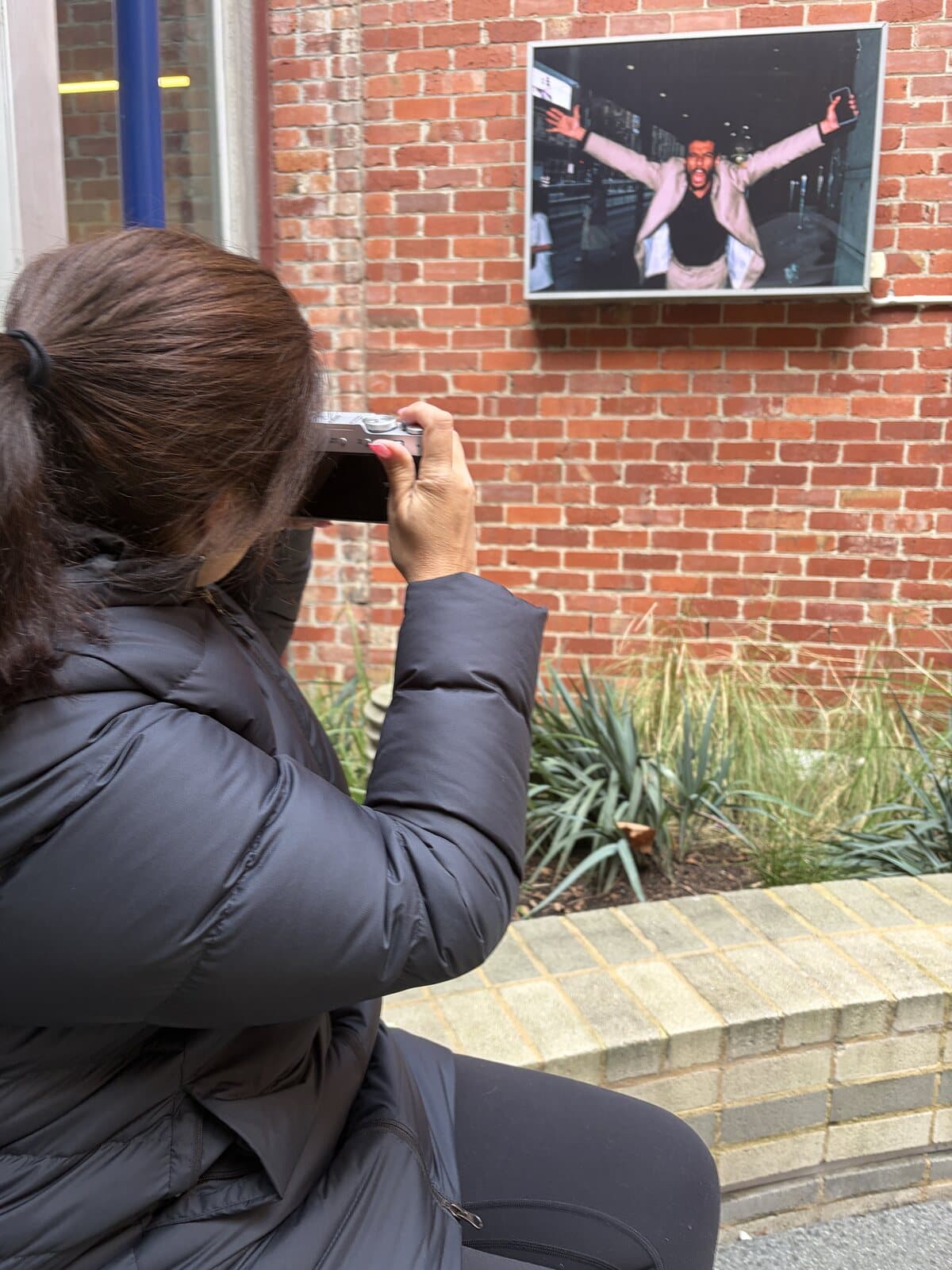 Penny photographing a framed street photograph on a brick wall with her Fujifilm X100VI during a Melbourne CBD photography course