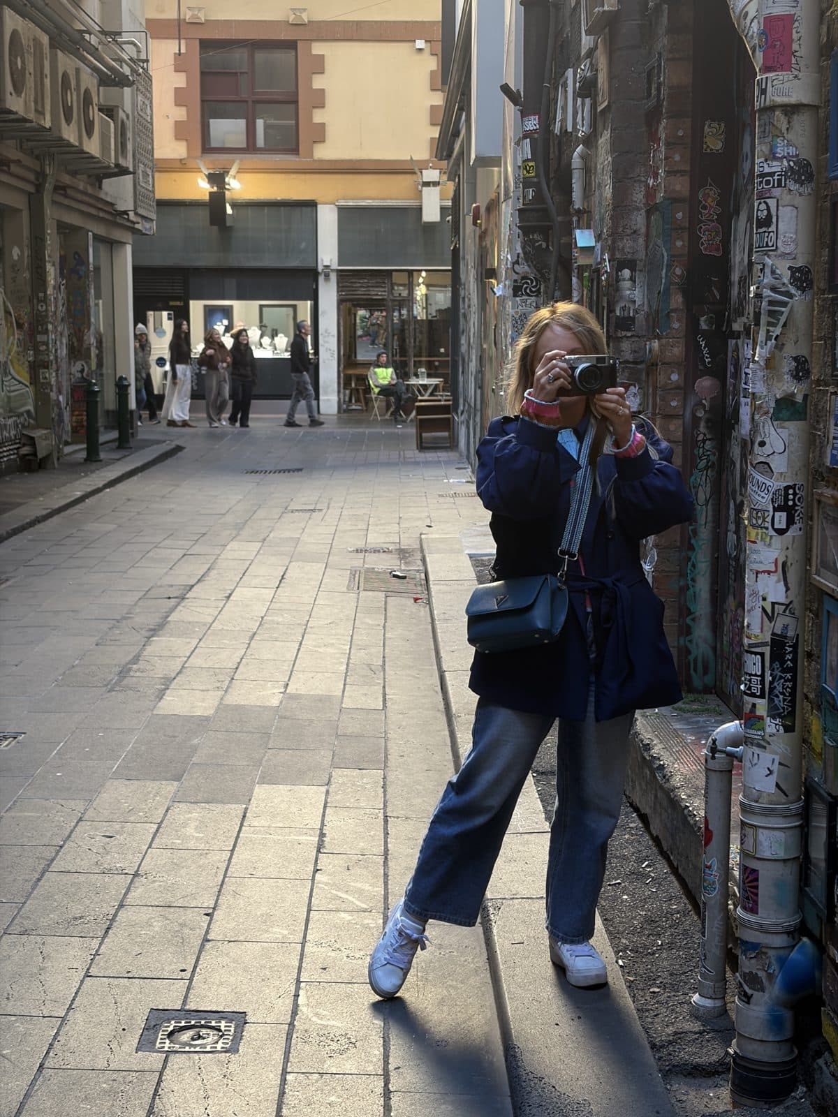 Rachael photographing a sticker-covered laneway wall with her Fujifilm X100VI during a Melbourne CBD photography course