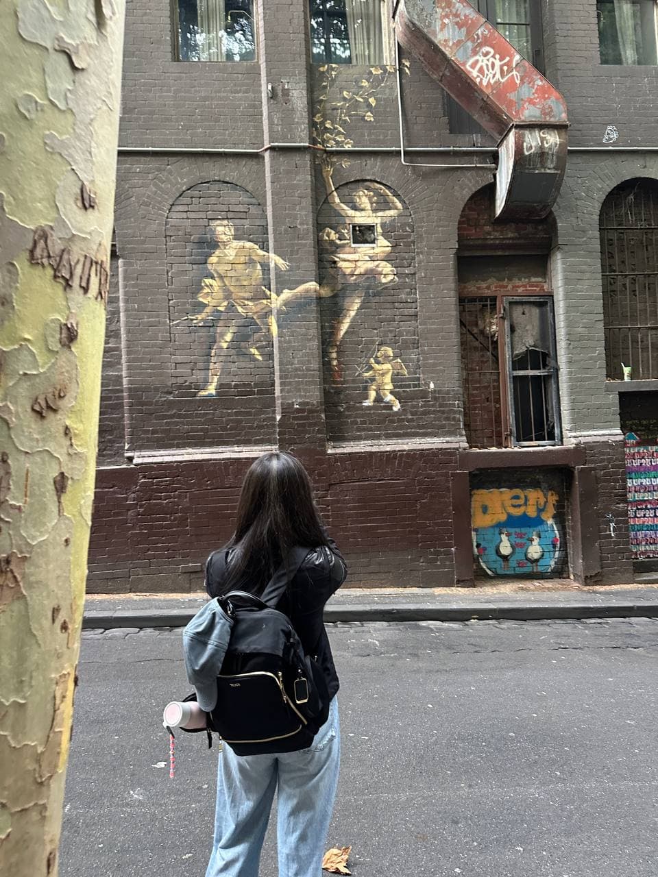 Janet standing in a Melbourne laneway photographing gold street art murals on a brick building during a photography course
