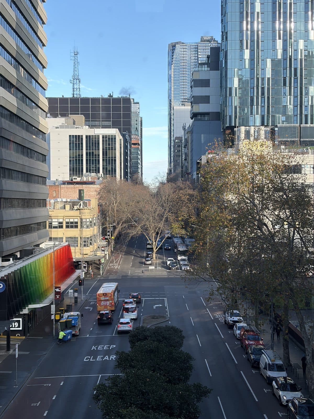 A rainbow-painted building facade on a Melbourne CBD street lined with plane trees, seen on the photography course walk