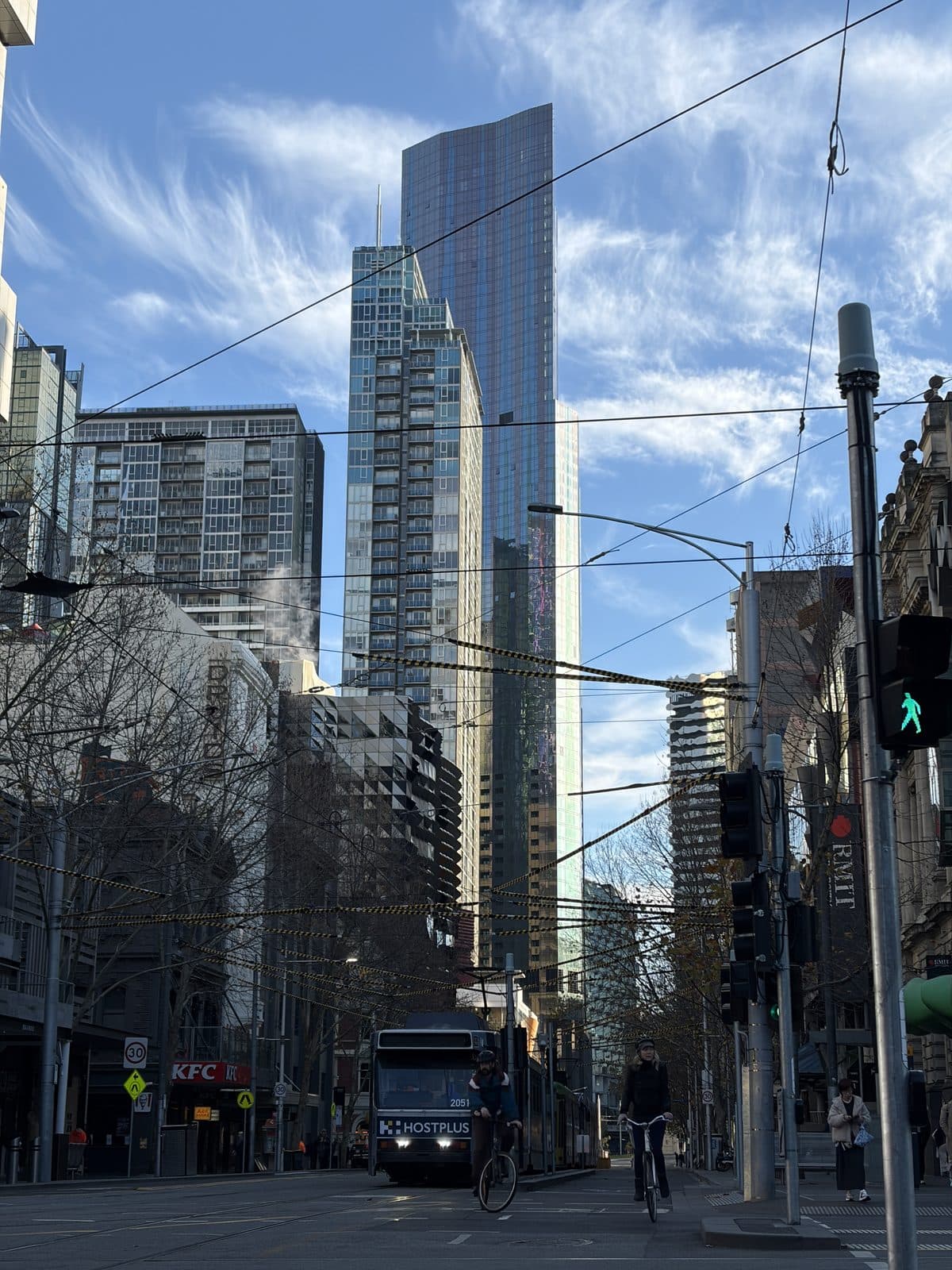 A Melbourne CBD street near RMIT with a tram, cyclists, and towers under a cirrus sky, a subject on the Sony A7 III photography course walk