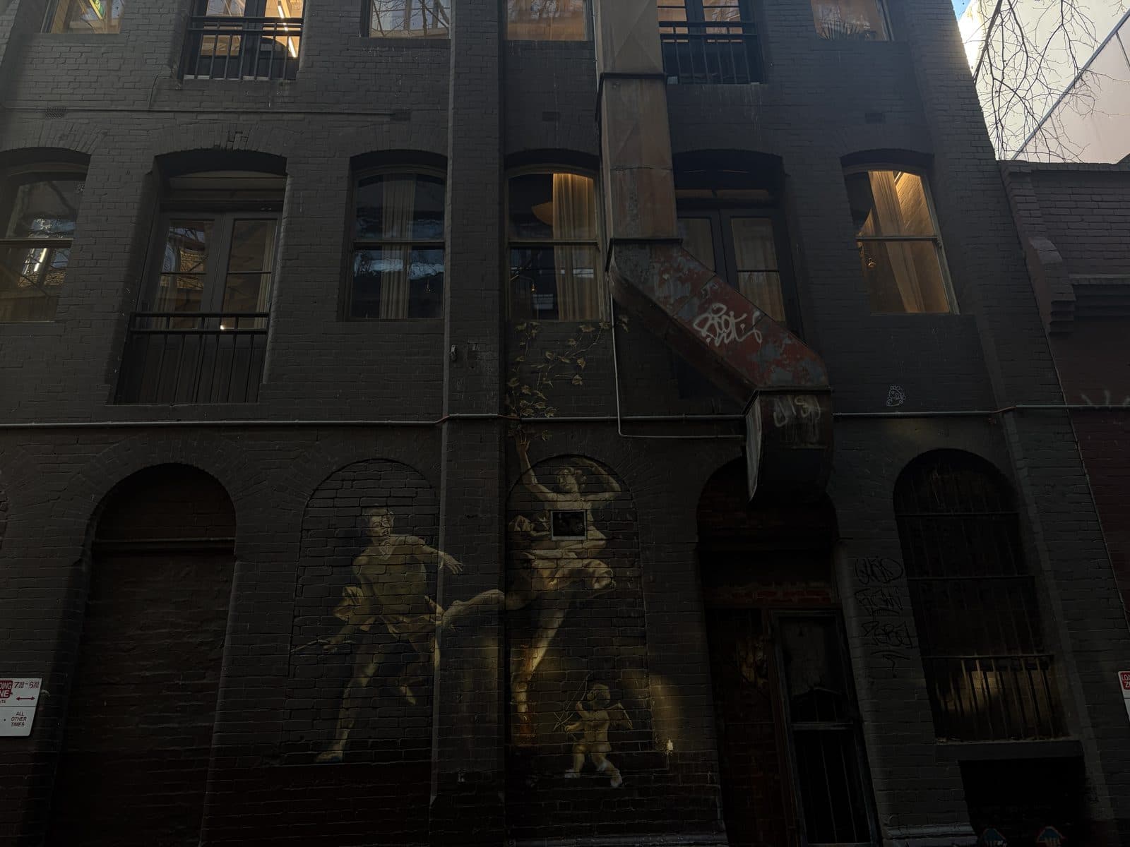 Gold-toned figures painted across the brick wall of a heritage building in a Melbourne laneway, a subject on the photography course walk