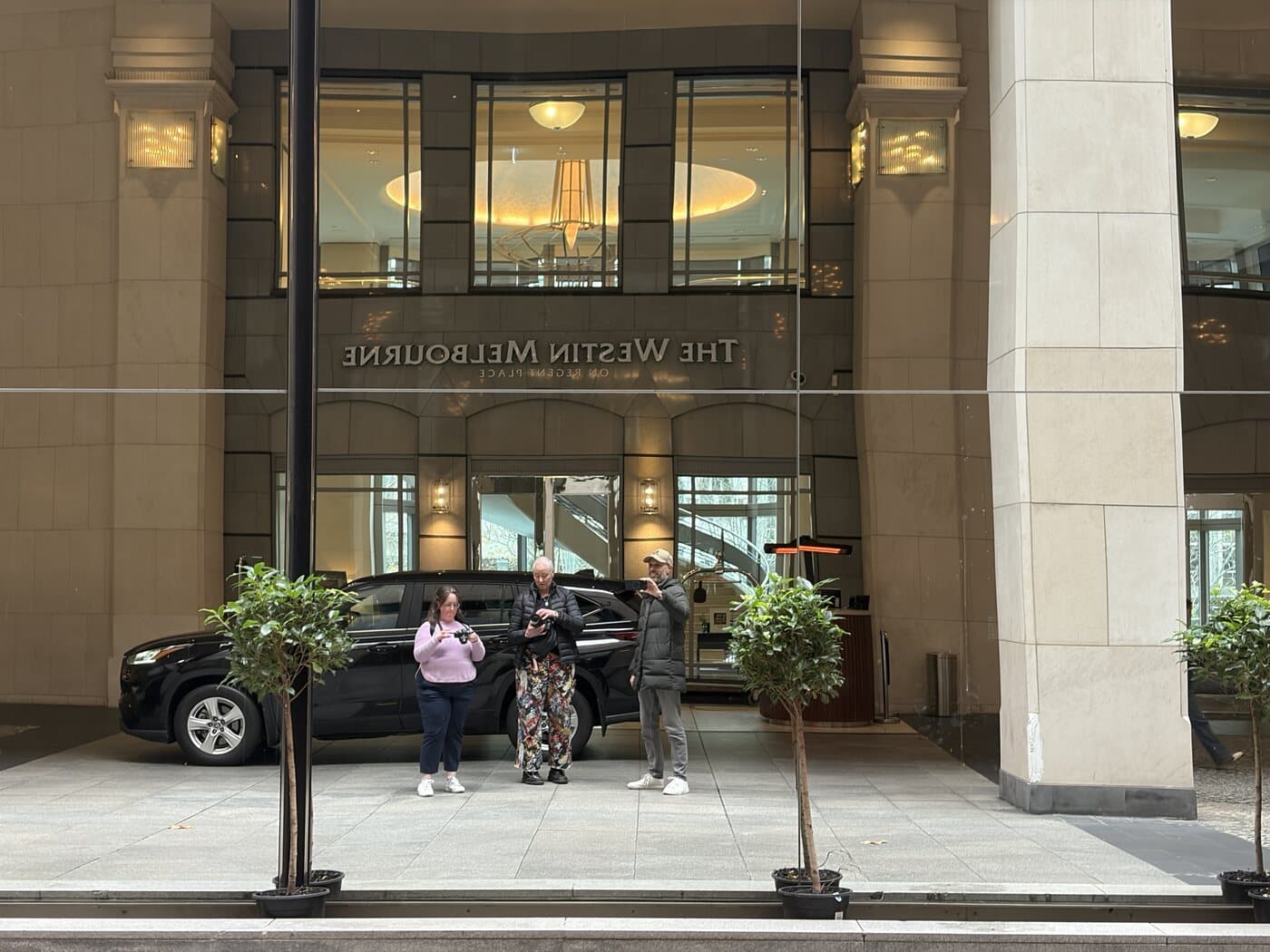 Daniel Bilsborough with students reflected in the mirrored glass facade of The Westin Melbourne during a photography course
