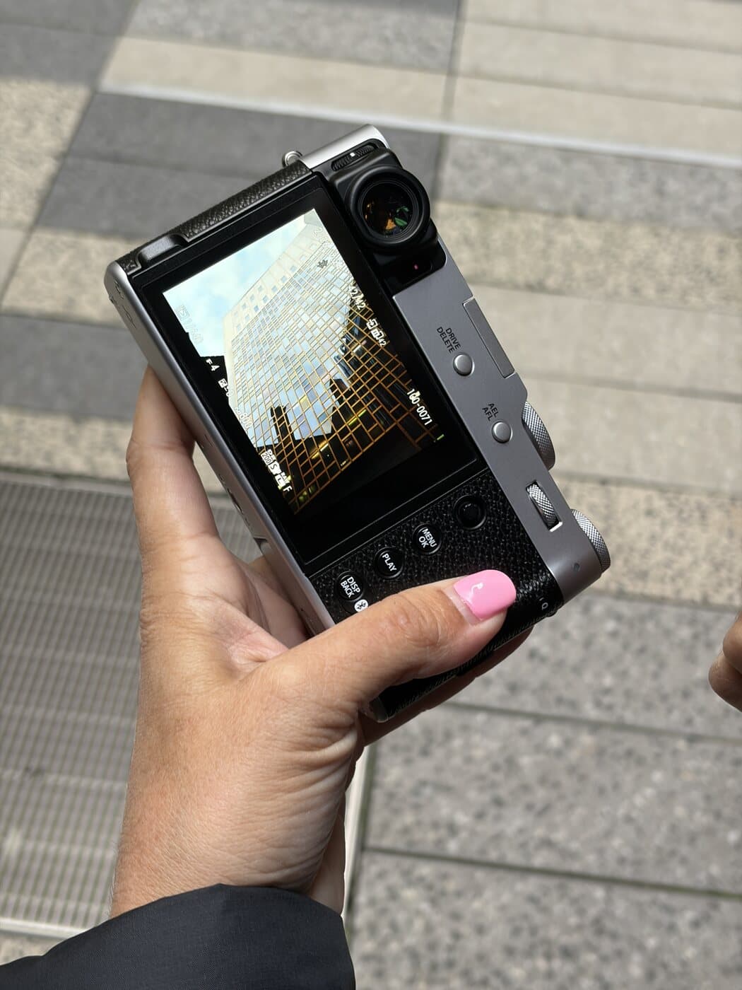 A Fujifilm X100VI held up to review a glass-tower shot at f/4 during a Melbourne street photography course