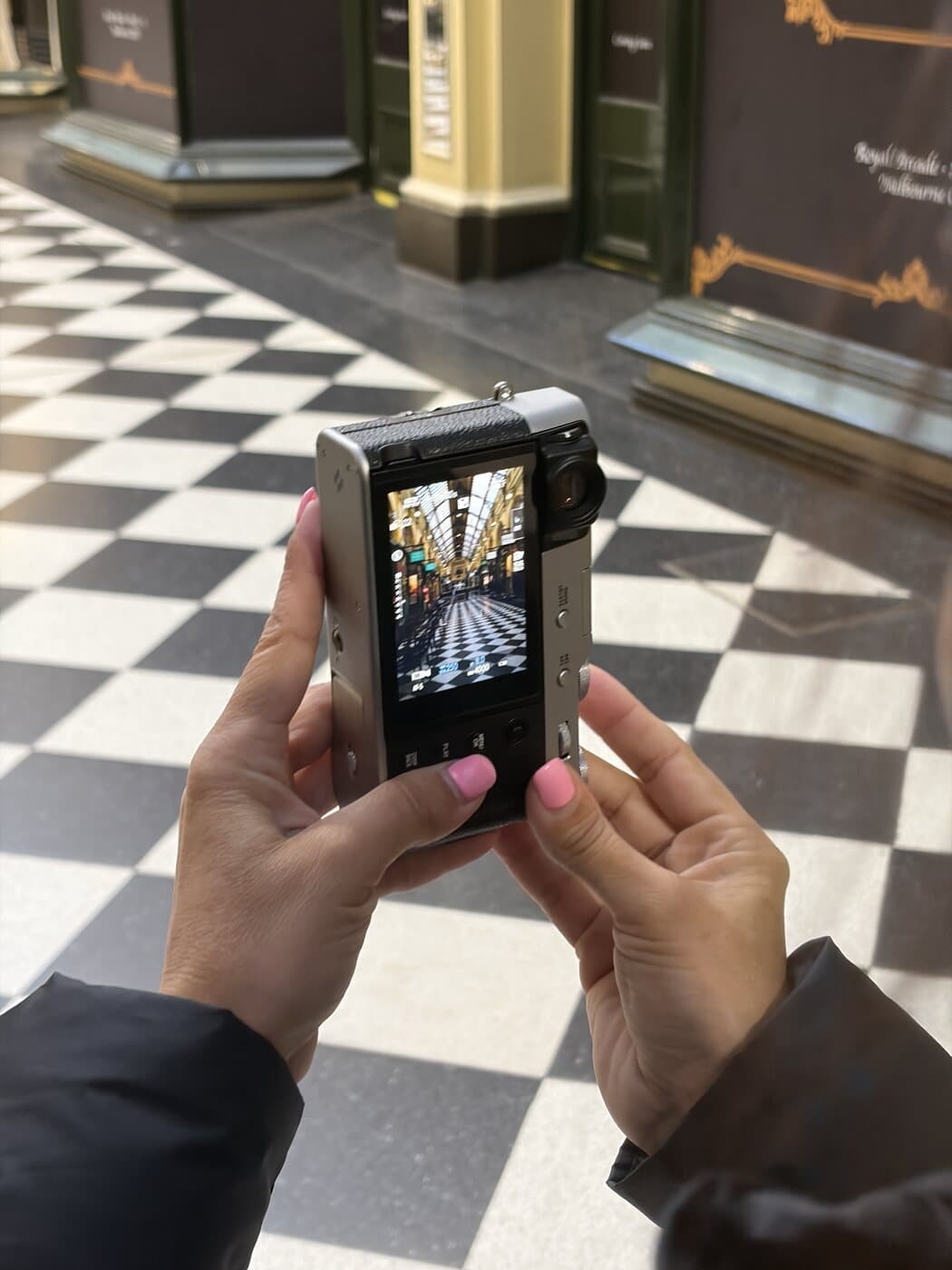 The rear screen of a Fujifilm X100VI framing the Royal Arcade in Melbourne, its checkerboard floor and glass roof in view