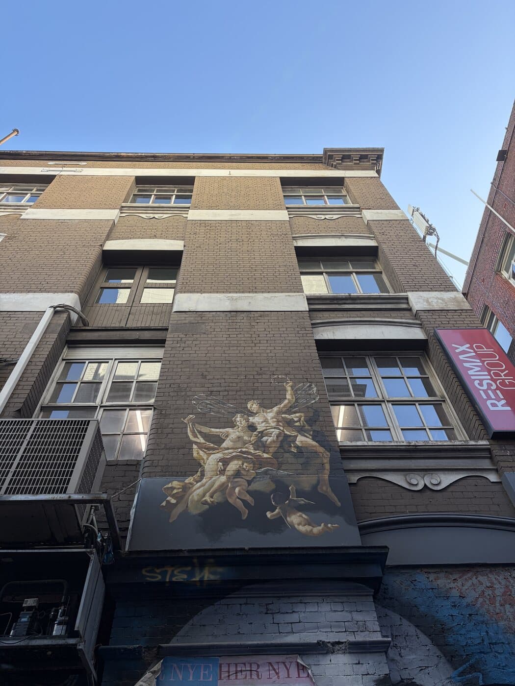 Looking up at a heritage brick building in Melbourne CBD with a classical painted mural, clear winter sky behind