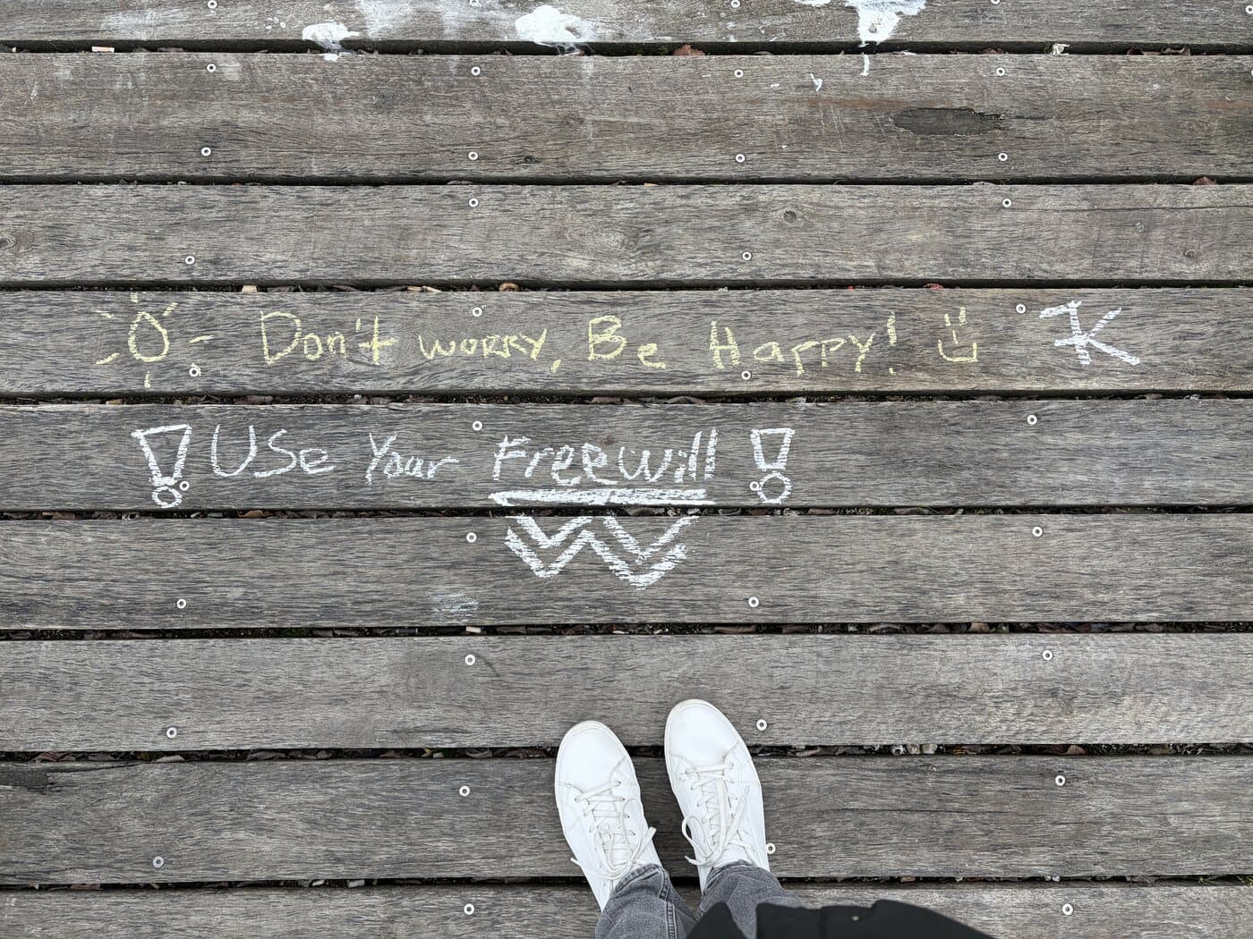Yellow and white chalk on a timber boardwalk reading Don't worry be happy, use your free will, photographed on the Melbourne photography course