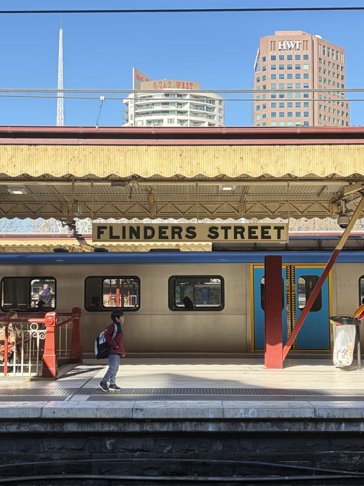 A boy on the platform at Flinders Street Station as a train pulls in, city towers behind under a clear winter sky, on the Melbourne photography course walk