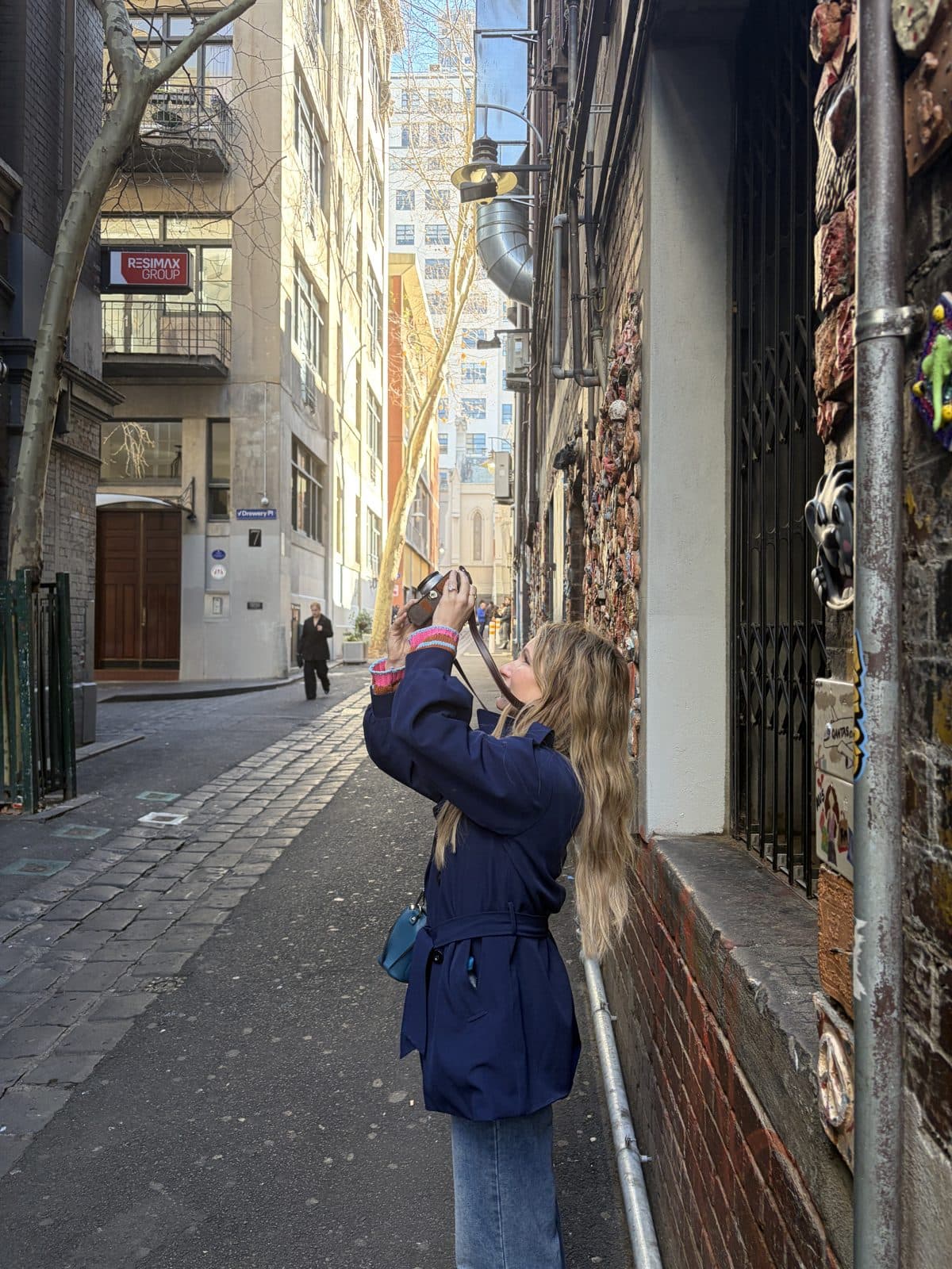 Rachael reaching up to photograph street art on a brick wall in a Melbourne CBD laneway near Drewery Place during the photography course