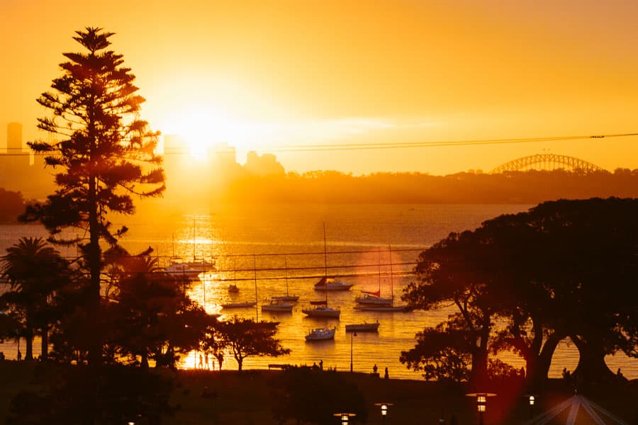 Golden hour sunset over Sydney Harbour with boats silhouetted against warm orange light, photographed by Daniel Bilsborough